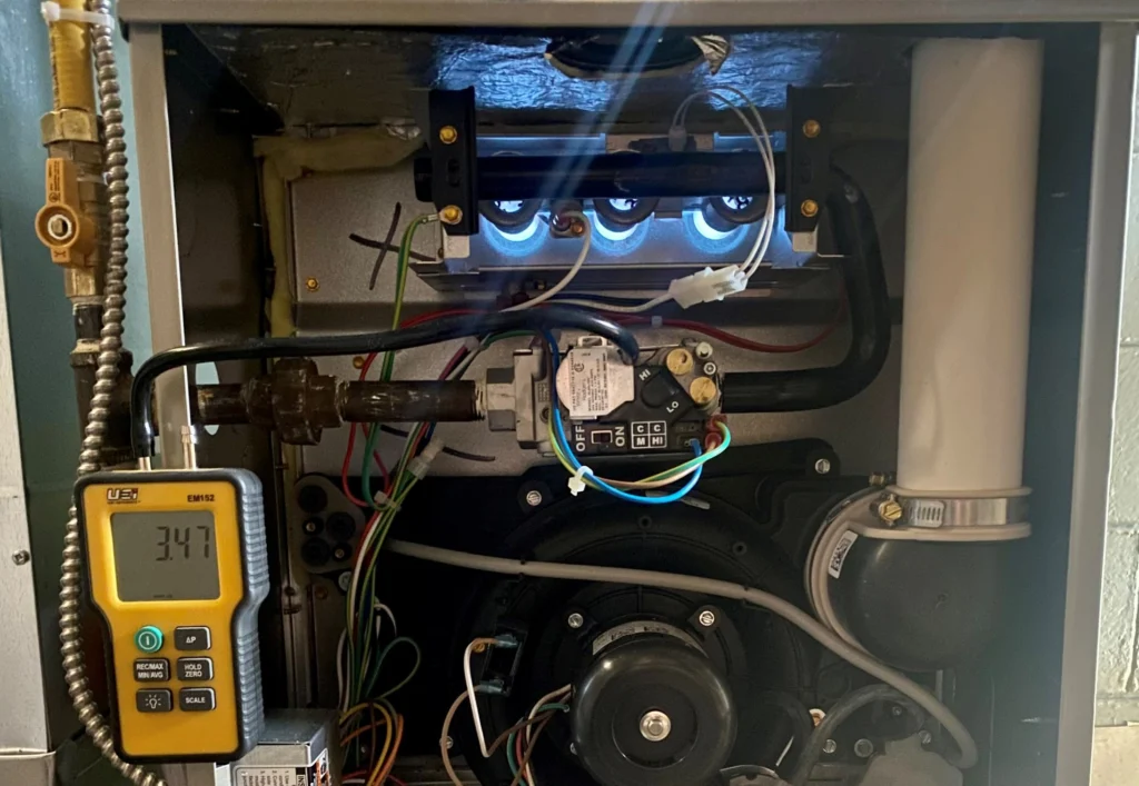 Technician testing gas furnace burner flames and pressure using a digital manometer during professional furnace repair and safety inspection