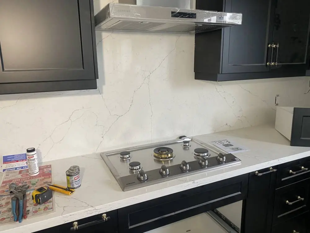 New stainless steel gas cooktop installed on white quartz countertop by HVAC Group in a modern kitchen with black cabinetry