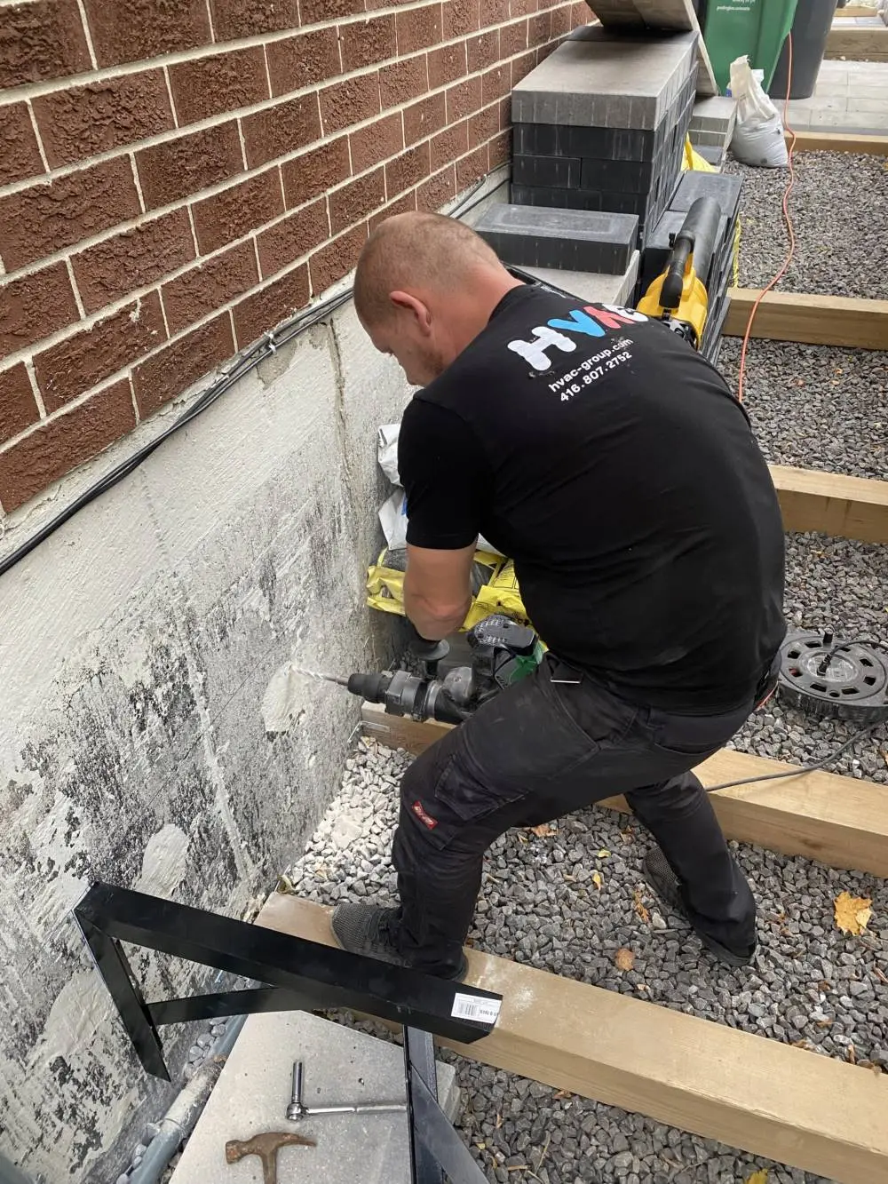 HVAC technician drilling into a wall to install a secure heat pump mounting bracket