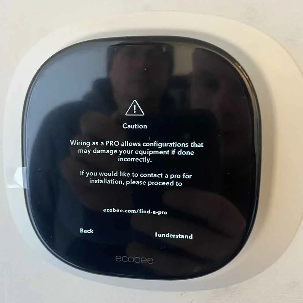 A close-up of an Ecobee smart thermostat displaying a caution message about professional wiring configurations to prevent equipment damage
