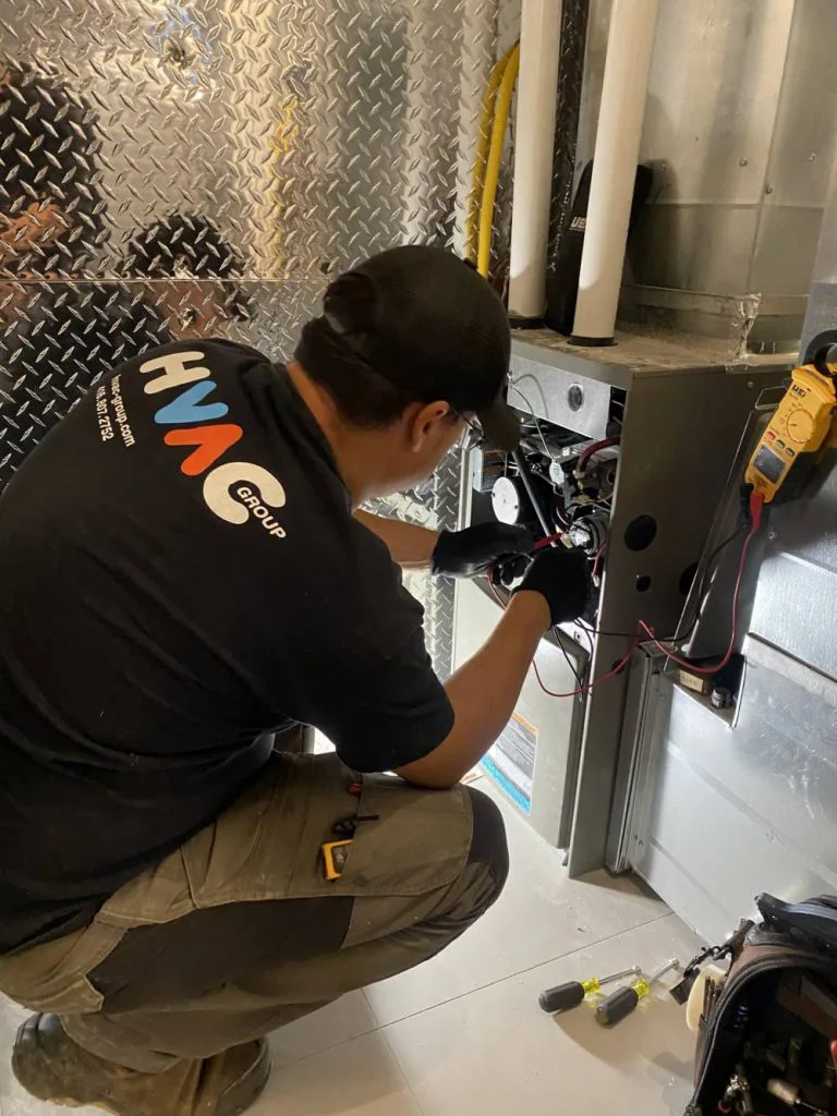 HVAC Group technician diagnosing a gas furnace with a multimeter during repair in Mississauga