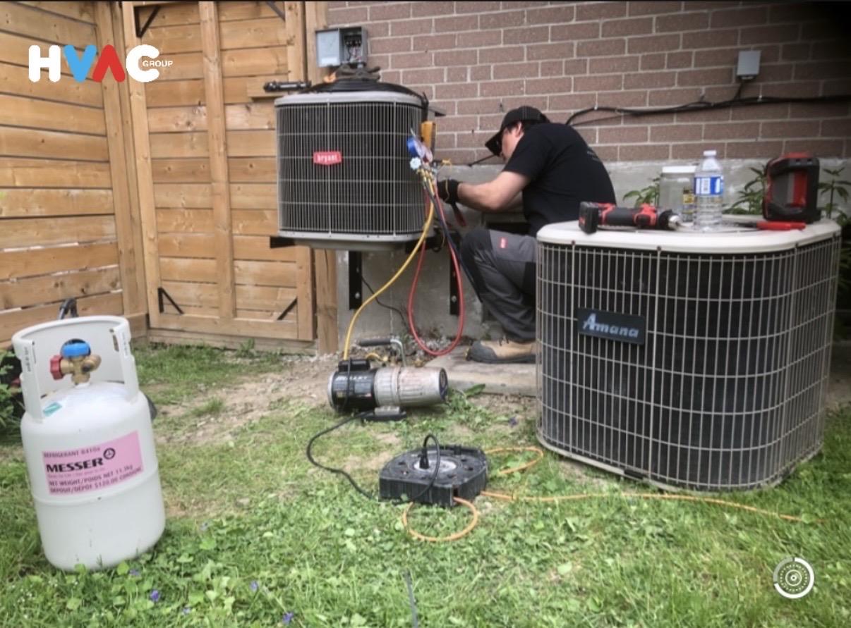 HVAC Group technician repairing Bryant AC with vacuum pump and R410A refrigerant beside Amana unit