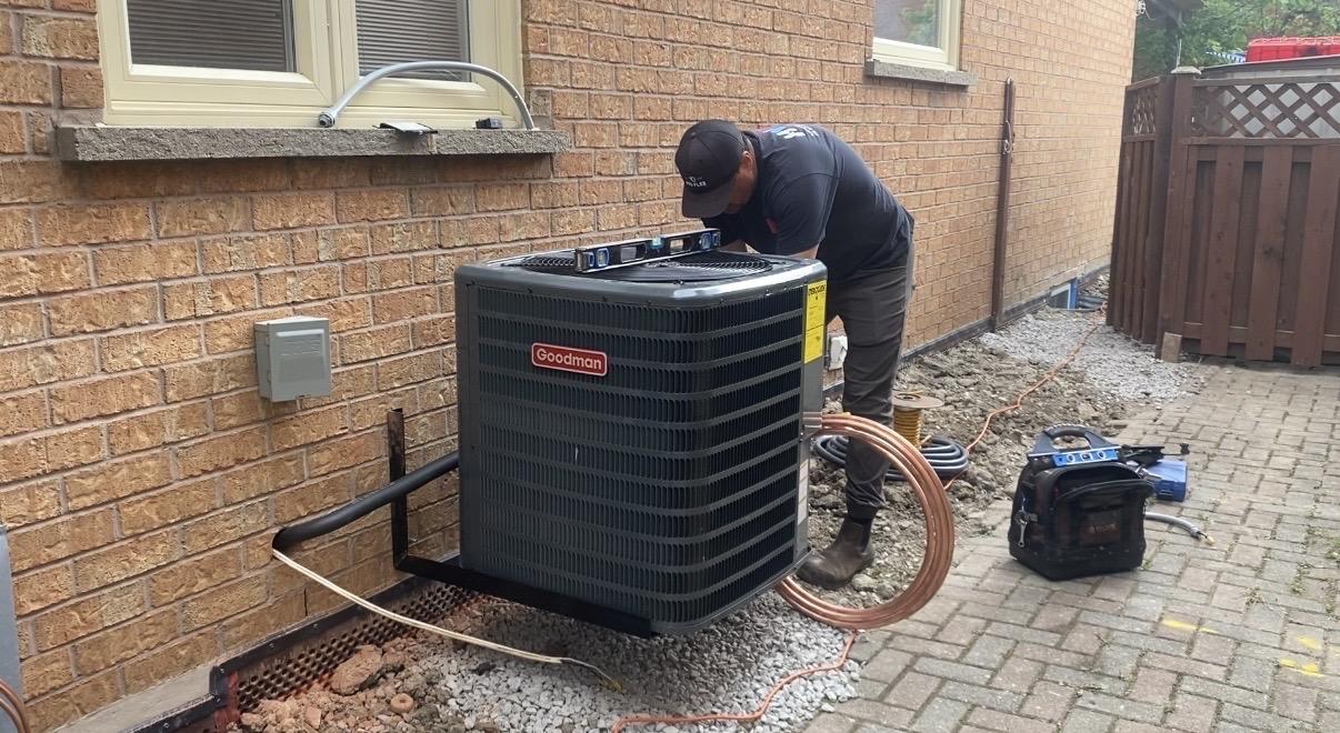 HVAC technician using a level on top of a wall-mounted Goodman air conditioner during installation
