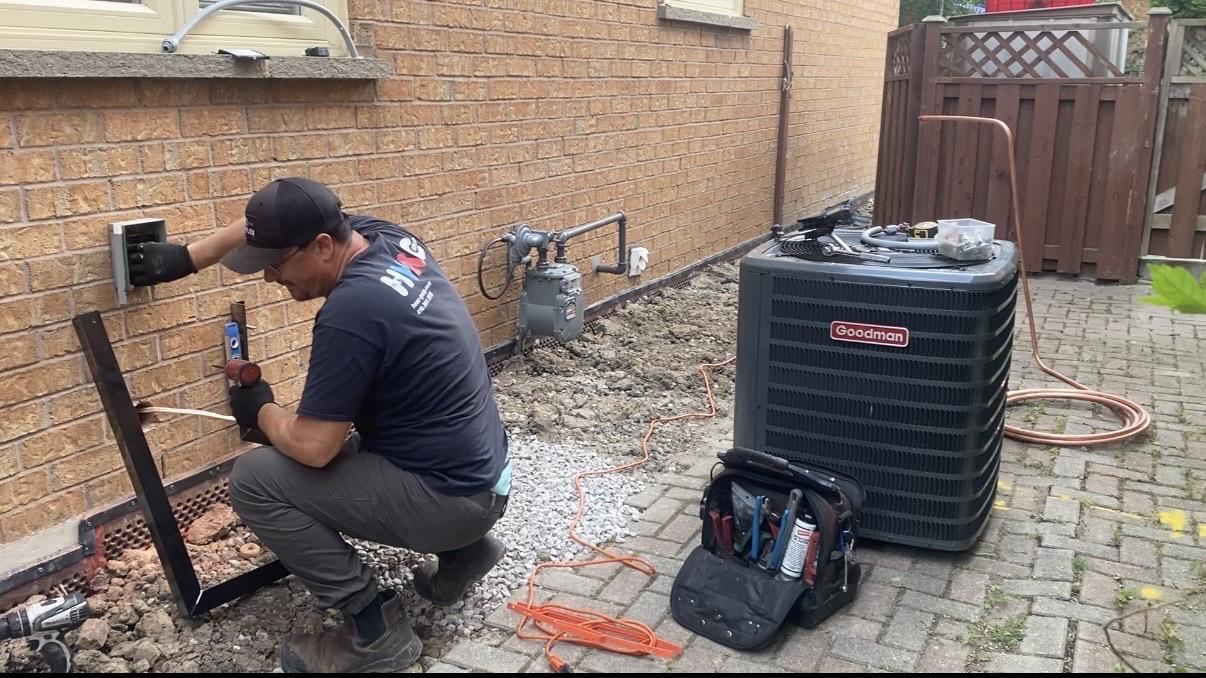 HVAC technician installing a Goodman air conditioner unit outside a brick residential building
