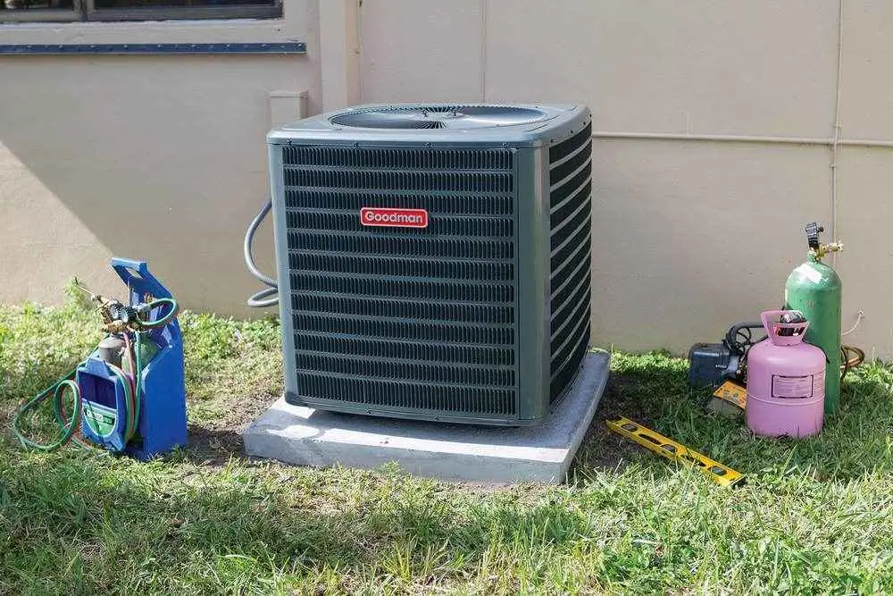 Goodman air conditioner on a concrete pad with refrigerant tanks and HVAC tools on the grass
