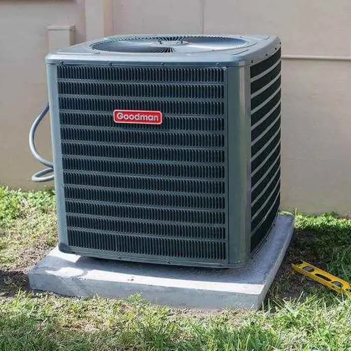 A Goodman air conditioner unit sitting on a level concrete base in a backyard with green grass