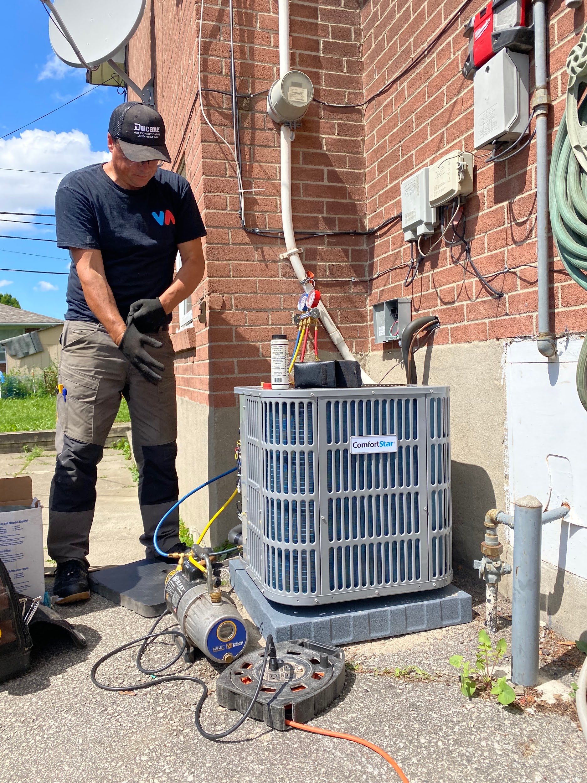 HVAC technician servicing a ComfortStar AC condenser with vacuum pump and manifold gauges at Mississauga home